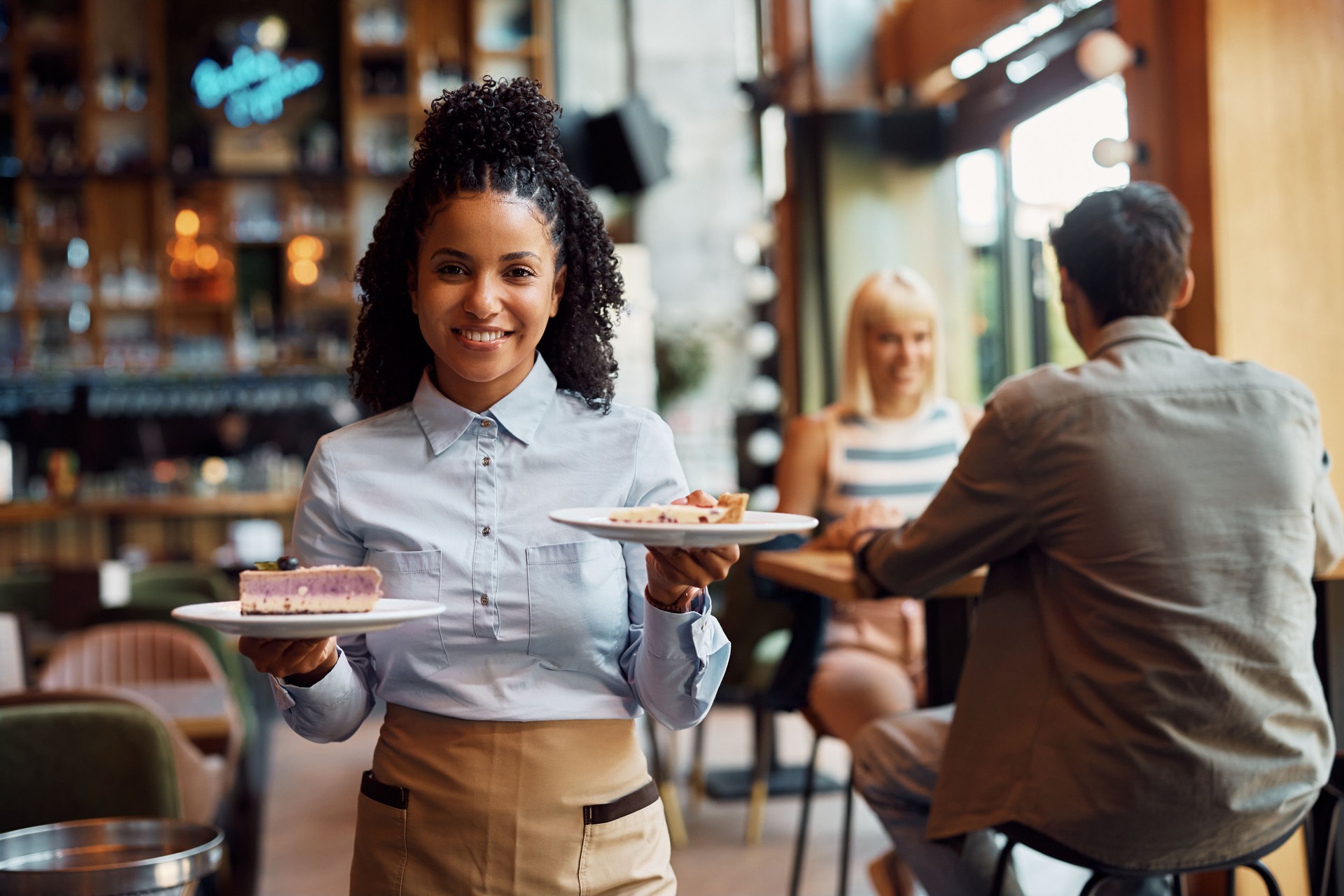Happy black waitress serving dessert in a cafe and looking at camera.
